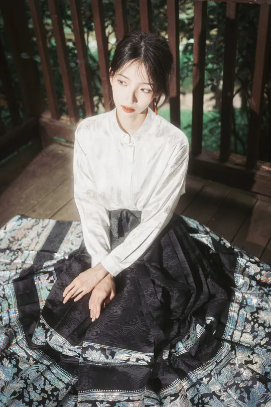 一个穿着白色衬衫和黑色裙子的年轻女子坐在门廊上