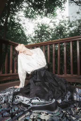 一个穿着白色连衣裙的女人躺在铺有黑白条纹床单和布料的木质甲板上