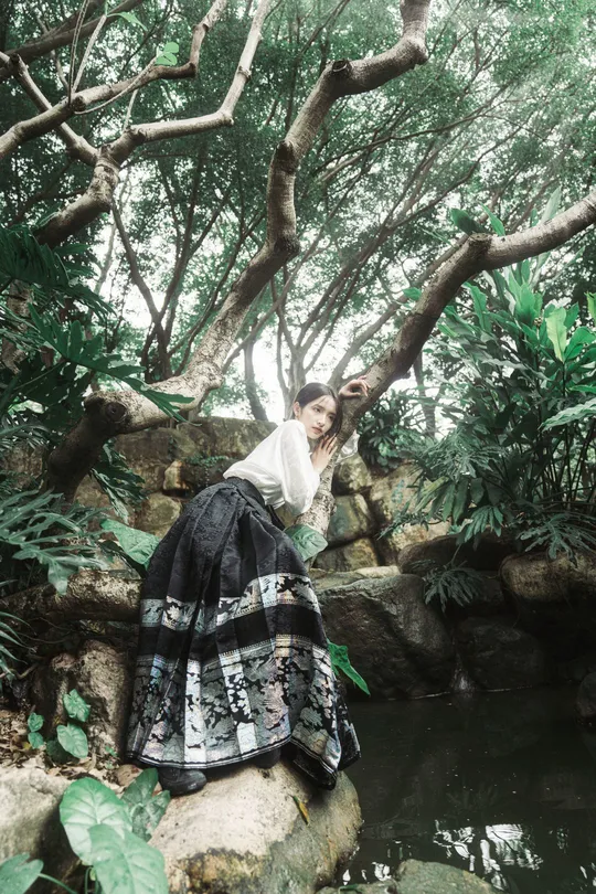 一个穿着黑白裙的女孩坐在靠近水塘的岩石上
