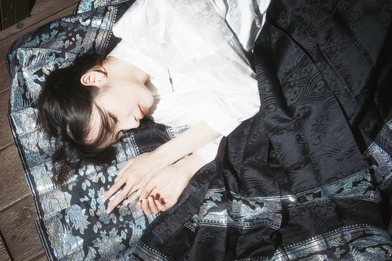 一个年轻女子躺在床上 盖着毛毯 一个箱子放在地板上。