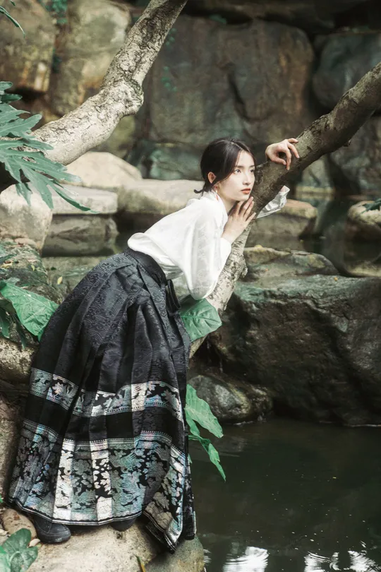 一位穿着美丽裙子的年轻女子坐在一棵树的树枝上 在水中。