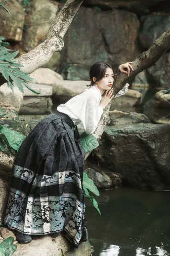 一位穿着美丽裙子的年轻女子坐在一棵树的树枝上 在水中。