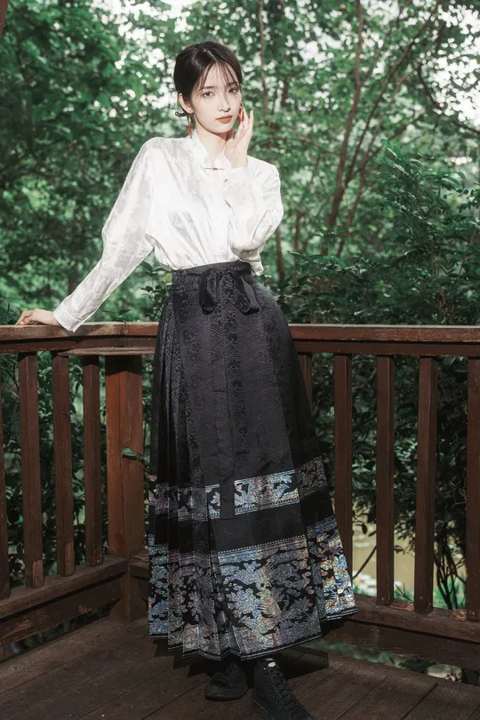 一位穿着黑色裙子和衬衫的年轻女子站在木质甲板上