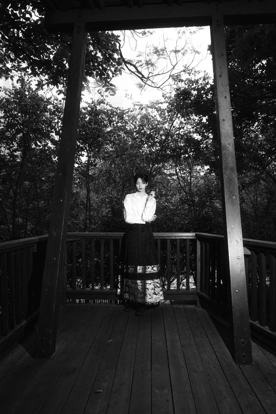 一个穿着连衣裙的年轻女孩站在门廊或甲板上 黑白照片