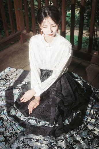 一个穿着白色连衣裙和黑色裙子的年轻女子坐在门廊上