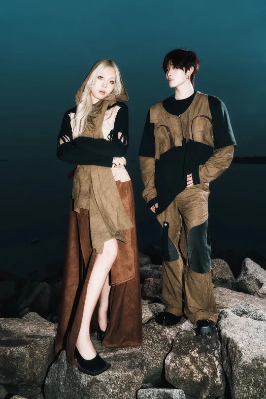 夜晚 一个年轻男子和一个穿着服装的女子站在岩石上 前方是水体。