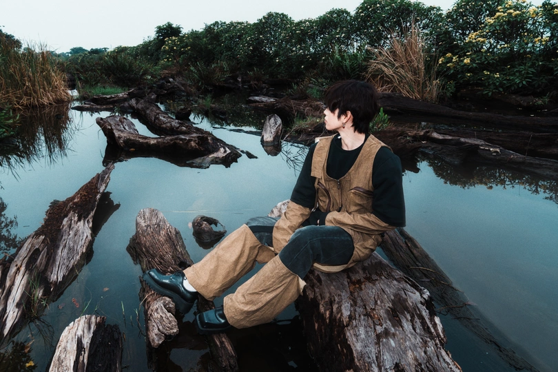 一位年轻男子坐在河中的树干上。