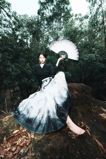 一位穿着连衣裙的女士在森林中的一块岩石上打着伞站立。