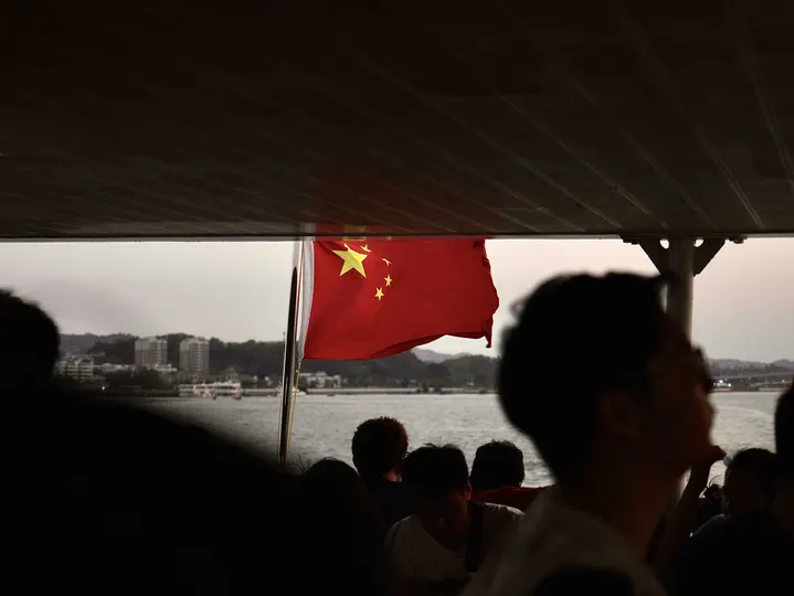 人们在船上看着一个在大片水域上飘扬的红旗。