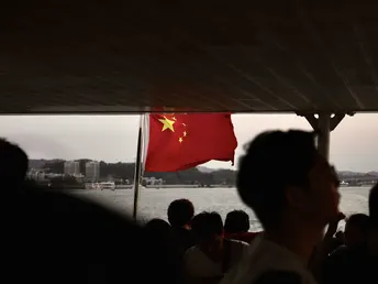 人们在船上看着一个在大片水域上飘扬的红旗。