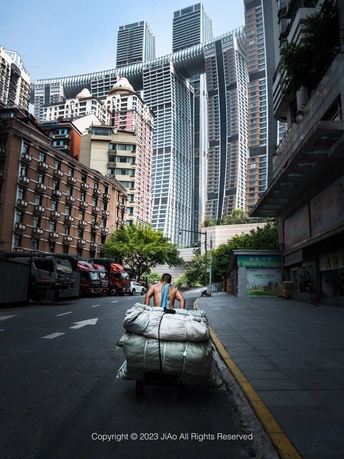 一个人推着装有大量行李的购物车穿过城市街道 街道两旁是建筑物。