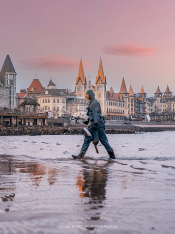 夕阳下 低潮时 有几个人在水中行走 背景是城市。