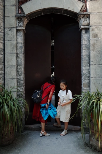 一个背着书包的女孩站在一栋建筑物的门口 而她的母亲走了过去。