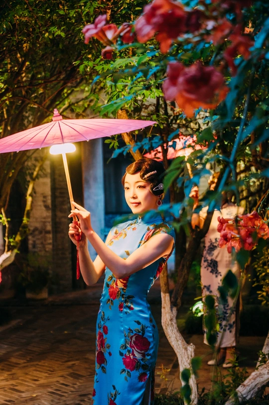 一位穿着传统蓝色连衣裙的年轻女子 手持粉色雨伞。