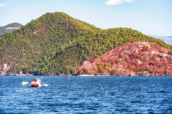 一片广阔的蓝色水域 中间有一艘小船 背景是山丘和山脉。
