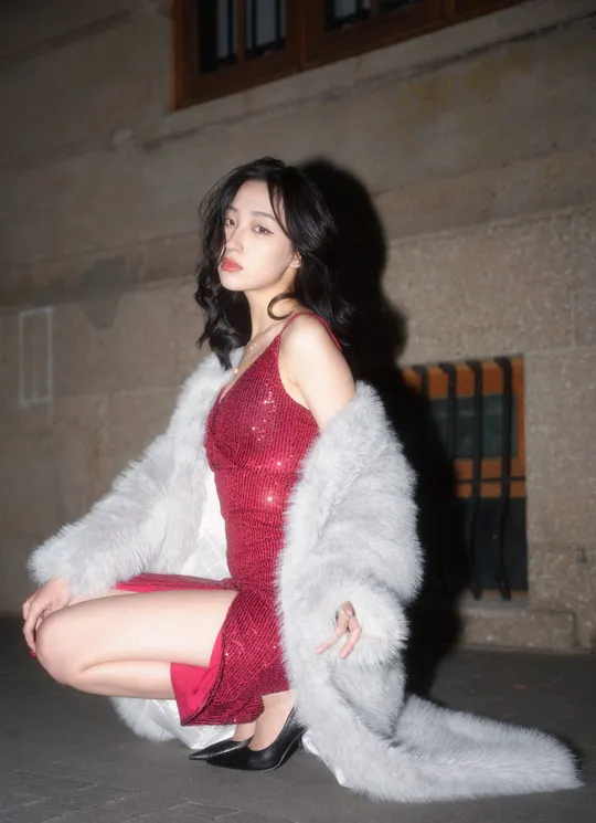 一位穿着红色连衣裙和白色靴子的女人坐在白色毛皮大衣前地上