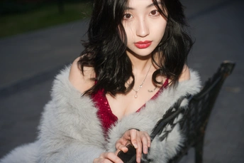 一位年轻女子穿着一件白色皮草大衣 手里拿着相机 坐在长凳上。