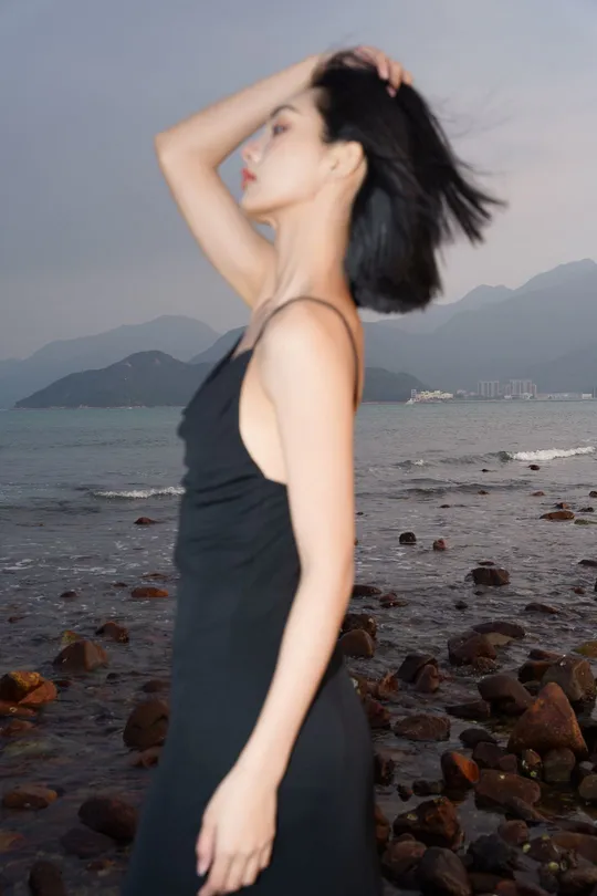 一个穿着黑色连衣裙的年轻女子站在靠近海洋的岩石上