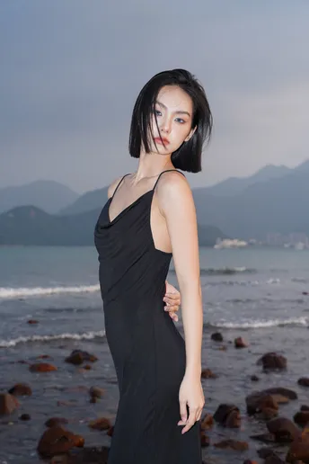 一位穿着黑色连衣裙的年轻女子站在靠近水边的海滩上