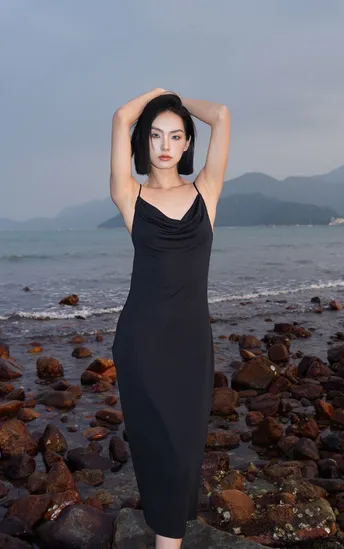 一位穿着黑色连衣裙的女人在海洋附近的海滩上摆姿势