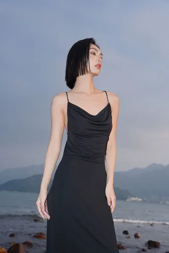 一位穿着黑色连衣裙的年轻女子站在靠近海洋的海滩上