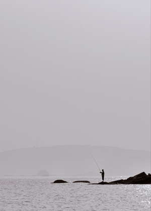 一个人站在水体中央的岩石上 远处有一艘船