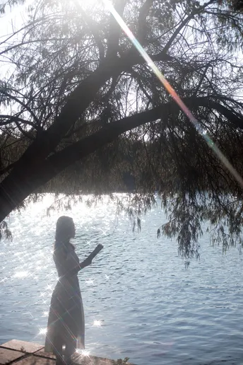 一位站在湖边码头上的女人 背景中有树和太阳