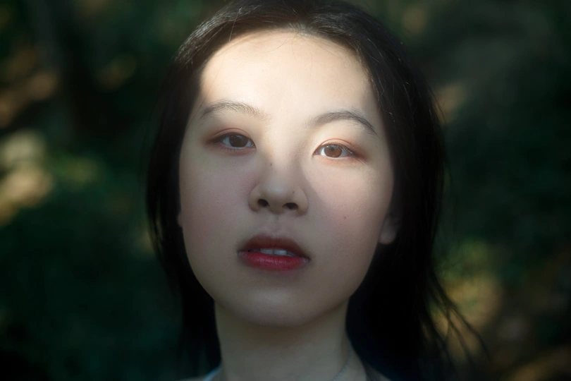 一位年轻女子站在森林中 面带严肃表情 凝视着镜头。