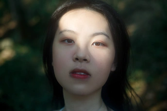 一位年轻女子站在森林中 面带严肃表情 凝视着镜头。