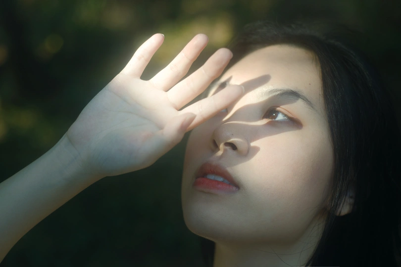 一位年轻女子举起手挡在脸上 让阳光照进她的眼睛