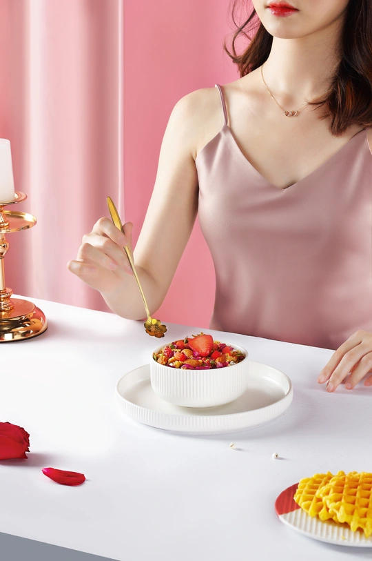 一位年轻女子坐在桌子旁 手里拿着一碗麦片、一盘草莓和其他食物
