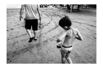 一个年轻男子沿着沙滩走 一个小男孩在沙子里玩耍。