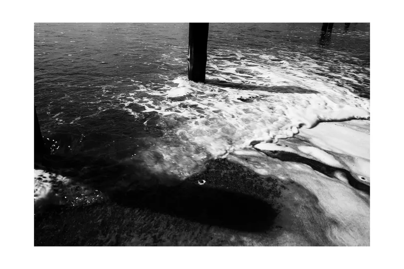 一张黑白照片 河上有波浪 有一个码头和一个电话杆。