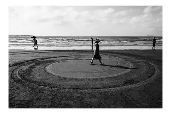一张黑白的海滩照片 人们在沙滩上行走 一个人站在圆圈的中心。