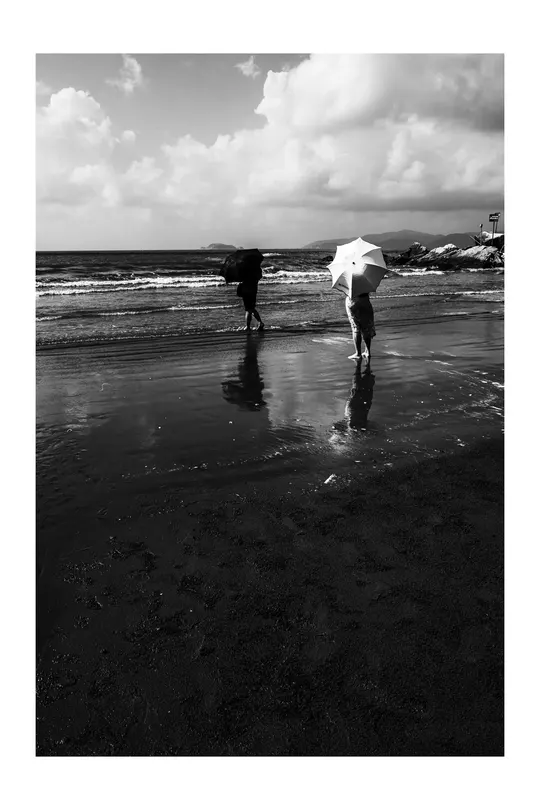 一个黑白海滩 一个人在水中行走 一个人拿着伞站在水中。