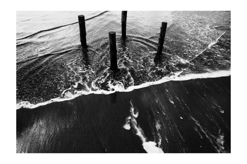 沙子和水中的一个码头和桩柱的黑白照片