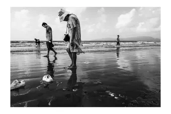 黑白照片上有人在海滩上行走 一个男孩站在水中。