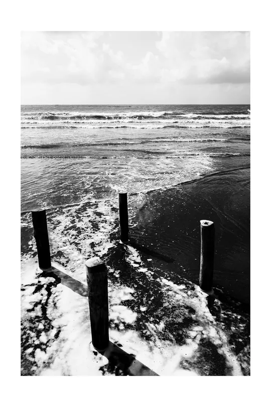 一张黑白的海滩照片 前景有杆子和柱子 背景有波浪。