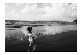 一个小女孩在沙滩上拿着桶走水边