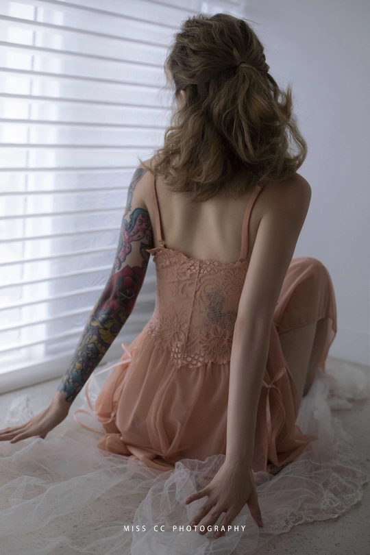 一个穿着粉色连衣裙的年轻女子坐在地板上看着窗外