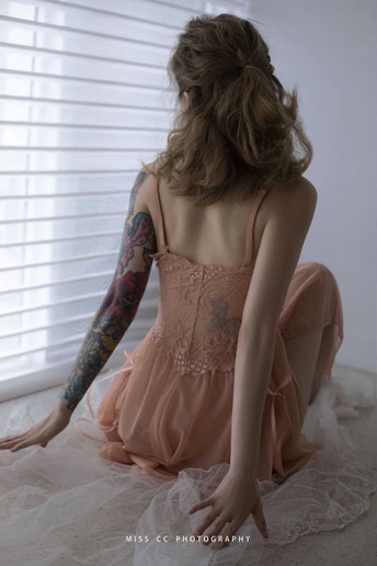 一个穿着粉色连衣裙的年轻女子坐在地板上看着窗外