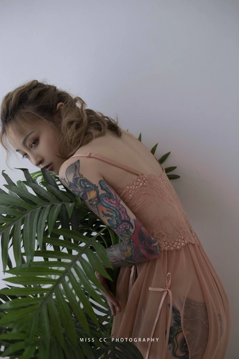 一个手臂上有纹身的年轻女子扶着一株靠墙的植物