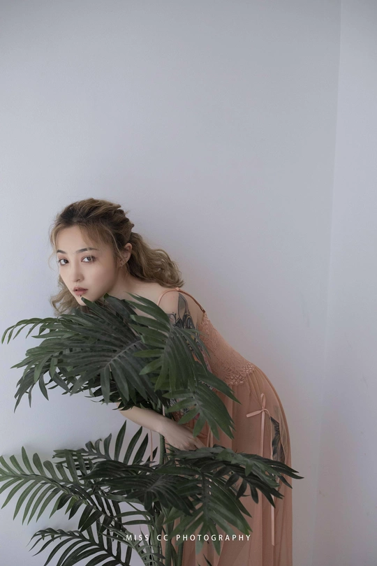 一个年轻漂亮的女人拿着一株绿色的植物靠墙站着