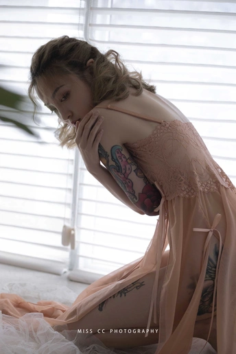 一位手臂上有纹身的年轻女子穿着粉色连衣裙在窗前摆姿势