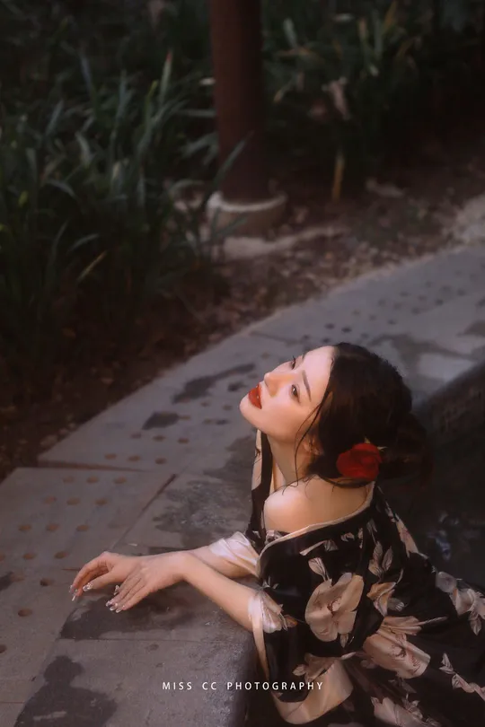 一个穿着连衣裙的年轻女子坐在人行道上 带着一把雨伞。