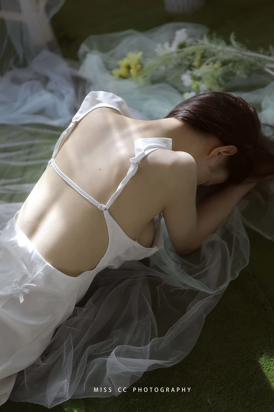 一位穿着白色连衣裙的年轻女子躺在床上