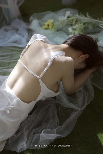 一位穿着白色连衣裙的年轻女子躺在床上