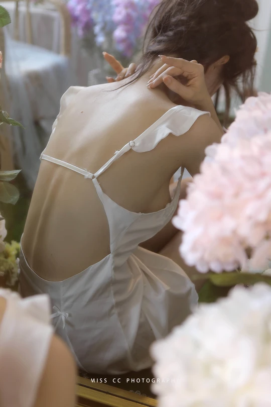 一位穿着白色连衣裙的年轻女子正在照镜子 镜子里有花。