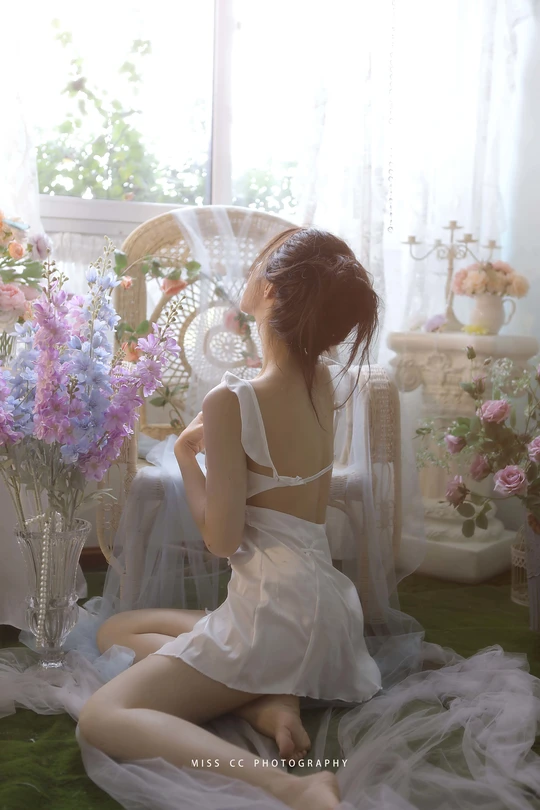 一个穿着白色连衣裙的年轻女子坐在花瓶旁边