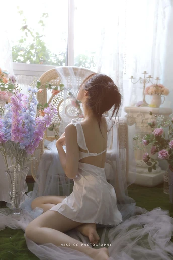 一个穿着白色连衣裙的年轻女子坐在花瓶旁边